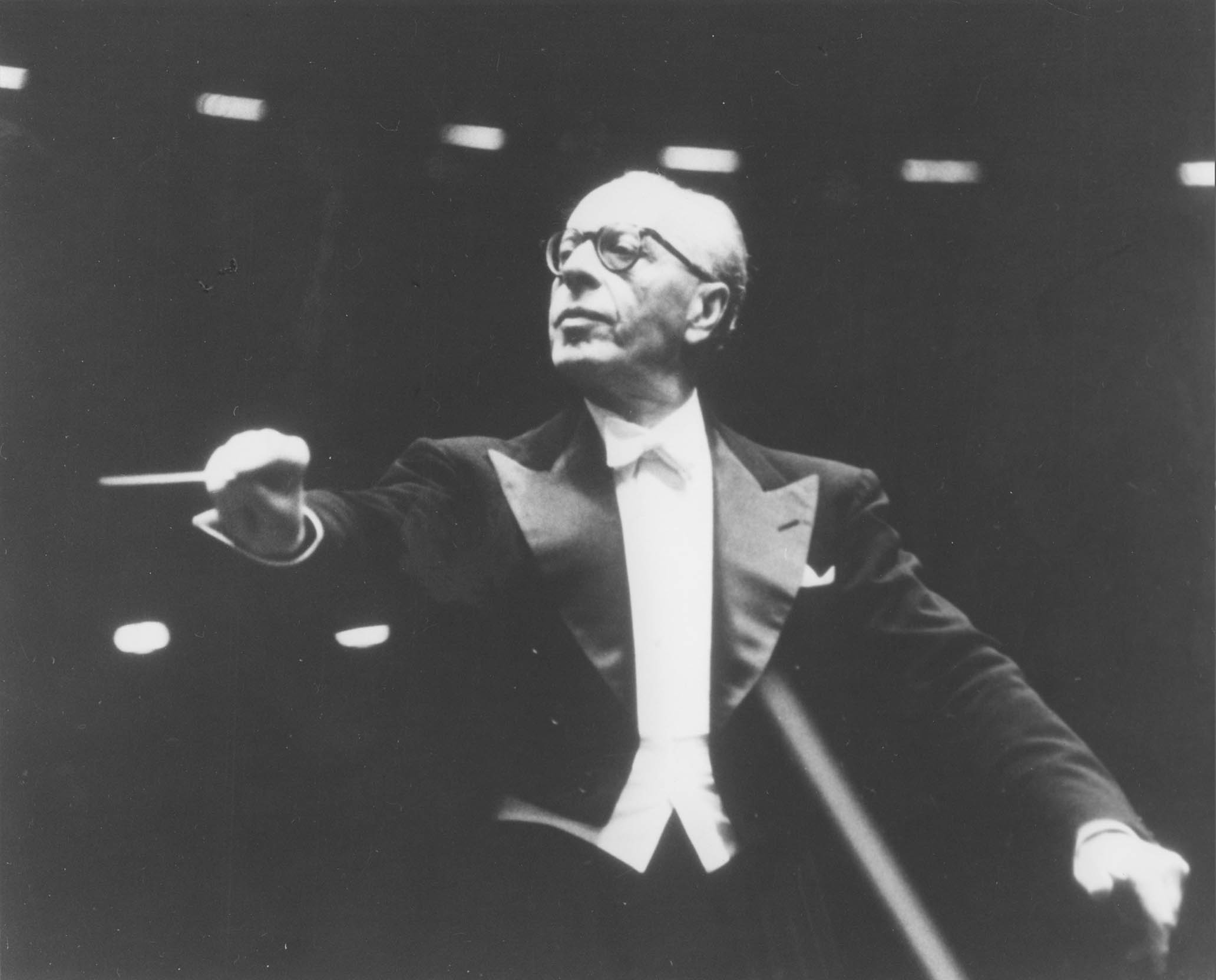 George Szell is conducting. He is looking to the left with a severe expression, and is dramatically cueing a performer.