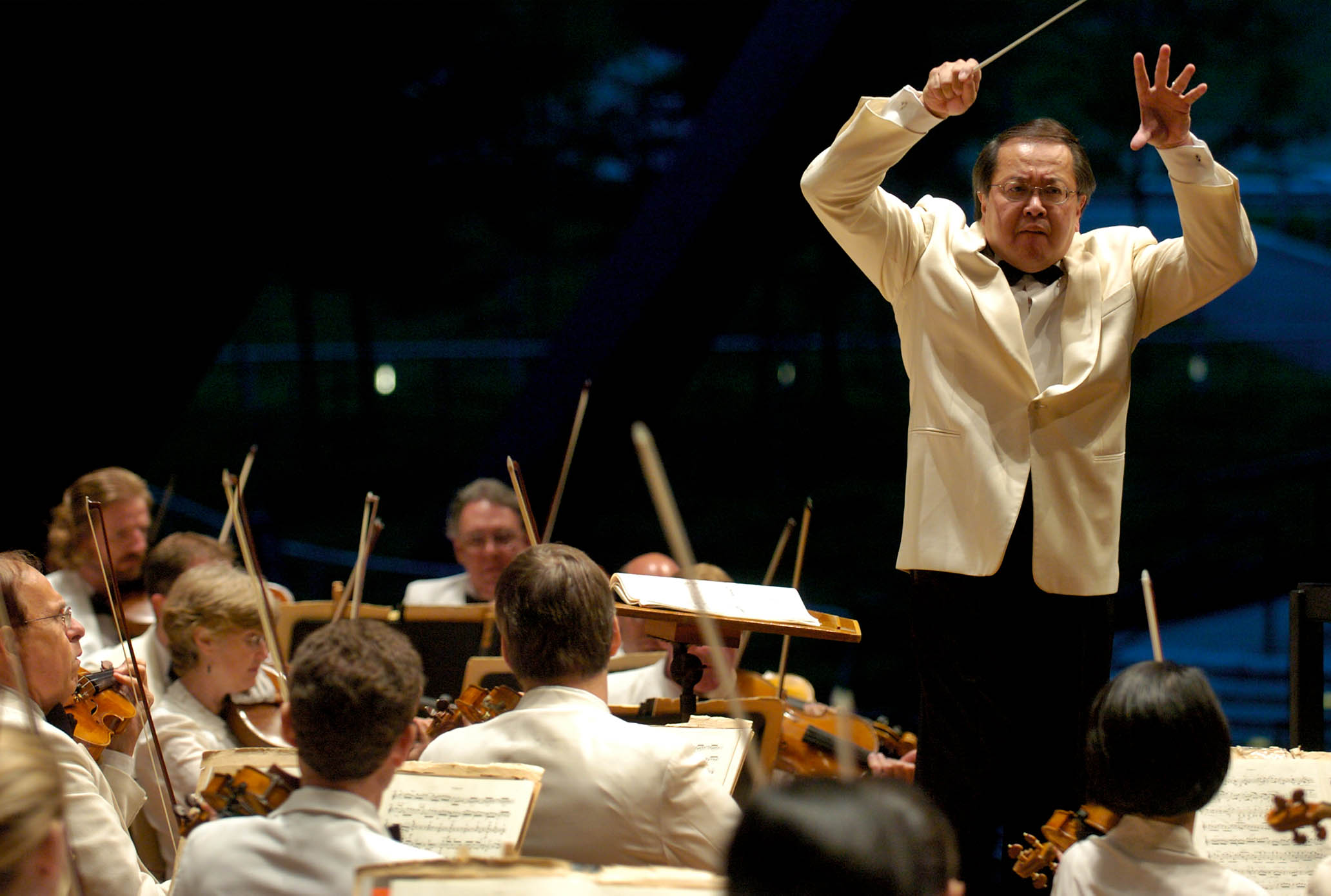 His hands held high, Jahja Ling conducts the Orchestra at Blossom. All are dressed in white jackets: formal dress for Blossom.