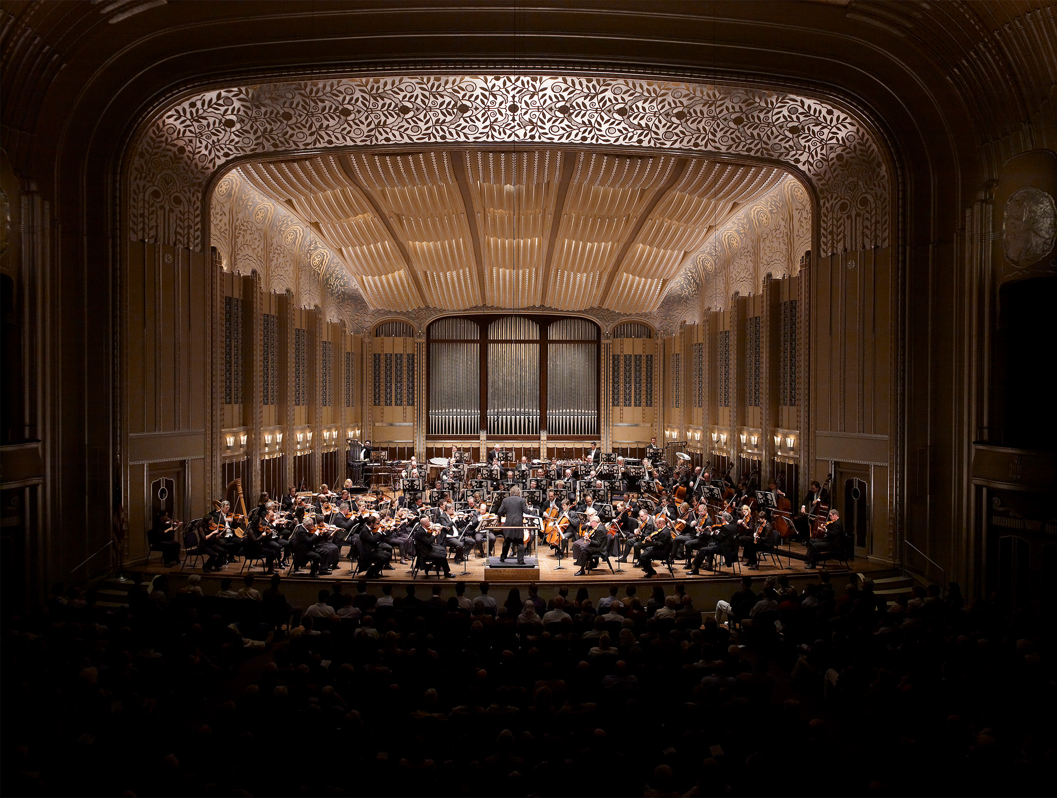 The Cleveland Orchestra, conducted by Franz Welser-Möst, is performing in Severance Hall. The photo shows the Orchestra and Franz animatedly performing and conducting, respectively.