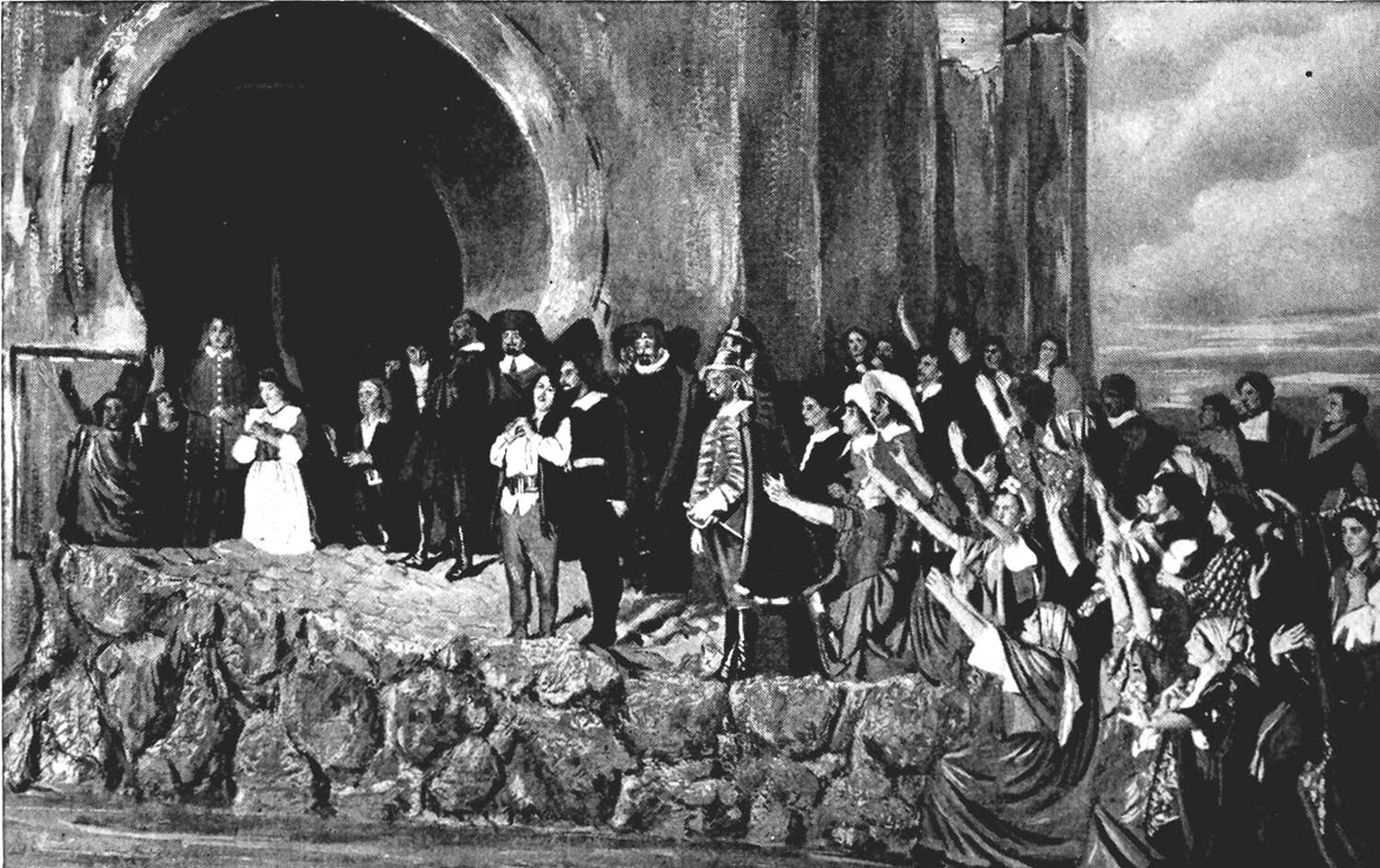 Leonora and Florestan are in the center, with Don Fernando on the side leading rescued prisoners in praise of Leonora’s bravery. They stand on rocky ground near water somewh along the base of the prison.  